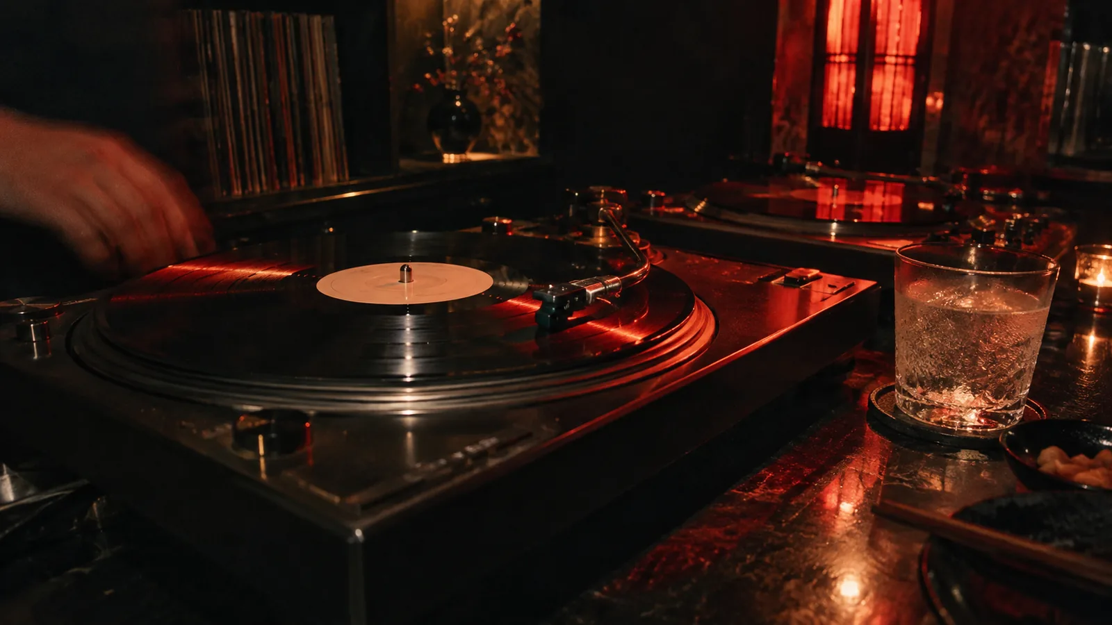 Turntables on a dark bar top, one record spinning under red light